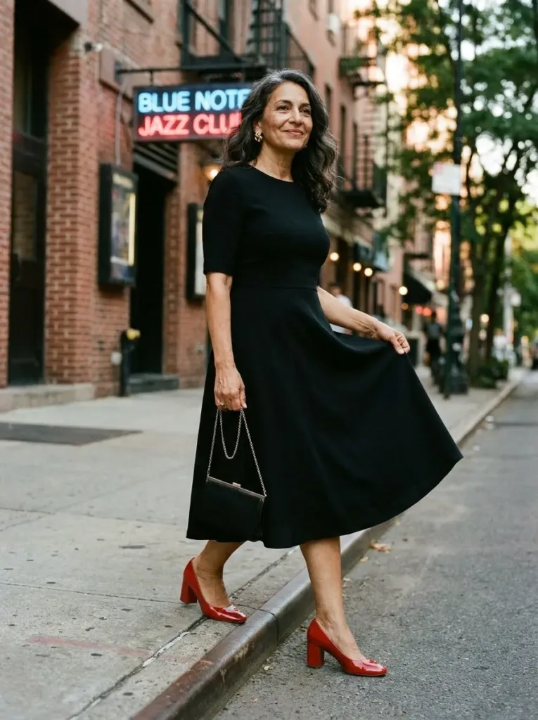 Woman over 50 in a black crepe bell-sleeve dress and red heels outside an evening party venue