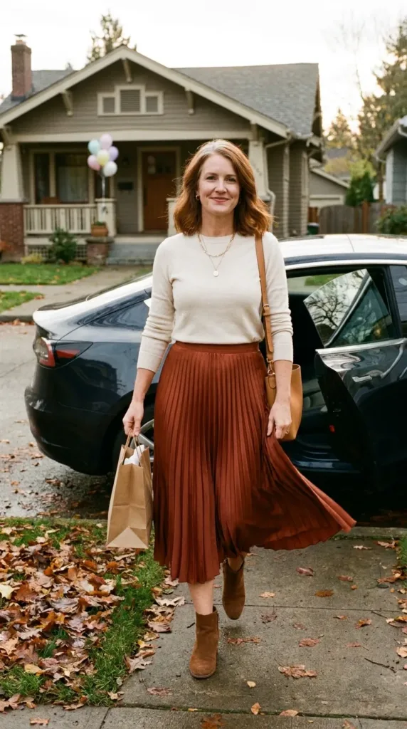 Woman in a rust pleated midi skirt and cream sweater, a fall baby shower guest outfit